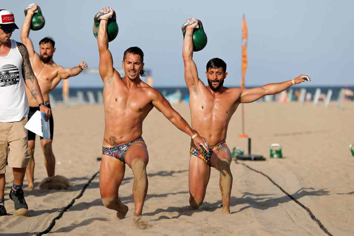 Atletas de crosffit practican en una playa italiana zancadas con pesas rusas.
