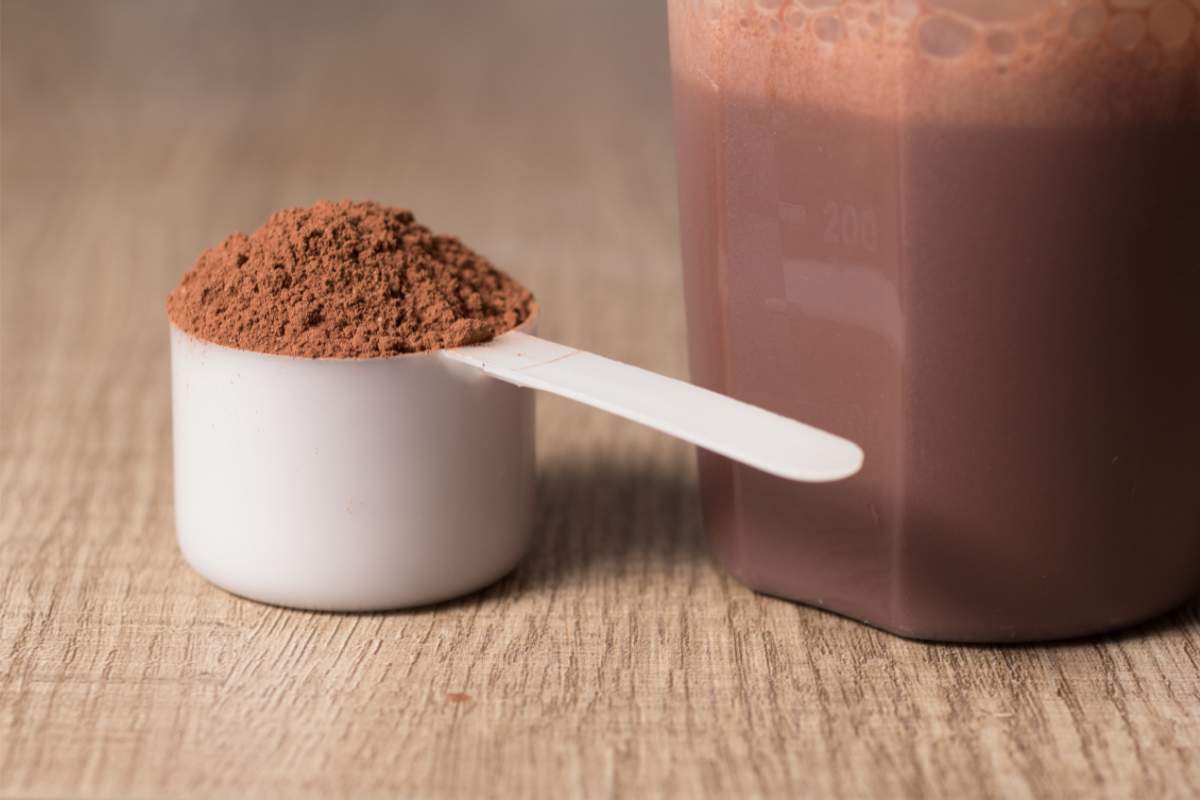 Scoop de proteínas de chocolate junto a un batido con agua de esos polvos.