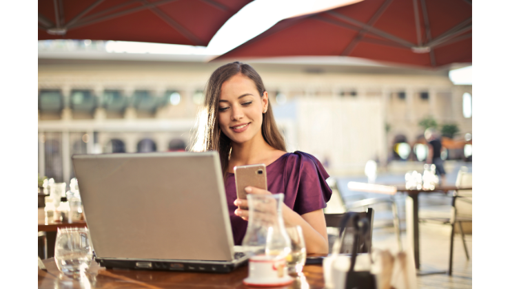 Una mujer en un restaurante con un portátil y un móvil. 