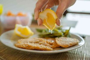 mano che mette limone su piatto di cotoletta