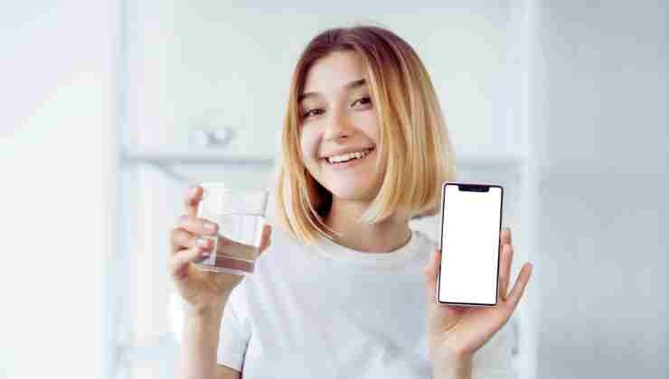 ragazza con bicchiere d'acqua e cellulare in mano