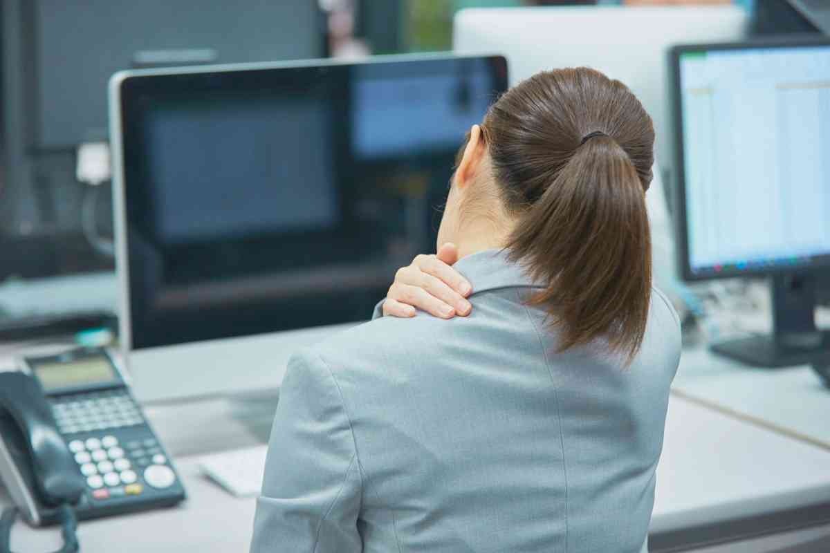 donna alla scrivania che si tocca la spalla