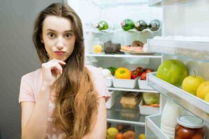 donna di fronte al frigorifero pensierosa
