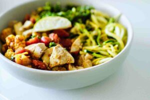 Insalata estiva con fettine di pollo grigliato, zucchine, rucola e crema di yogurt al limone, servita in un piatto chiaro con erbe fresche