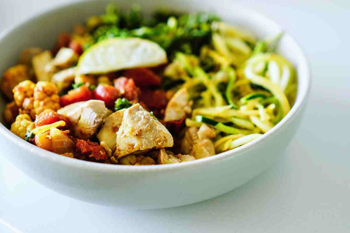 Insalata estiva con fettine di pollo grigliato, zucchine, rucola e crema di yogurt al limone, servita in un piatto chiaro con erbe fresche
