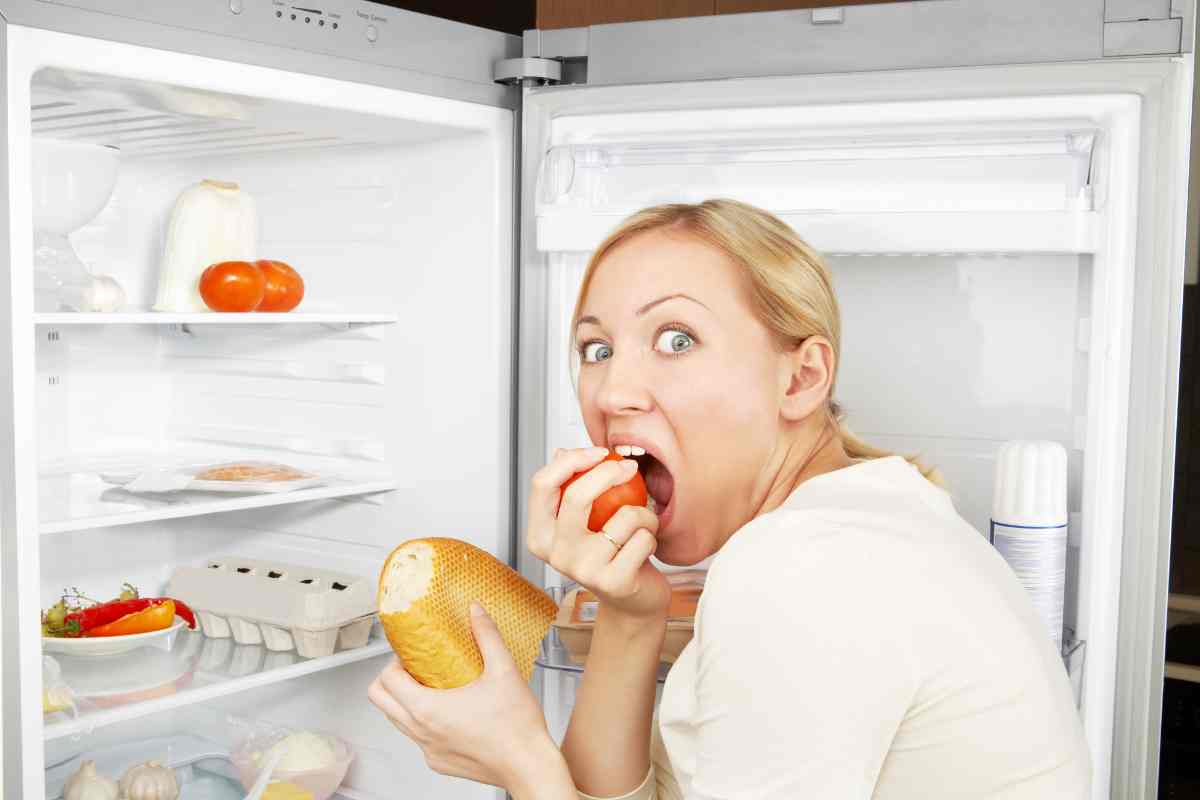 persona che mangia affamata di fronte al frigo