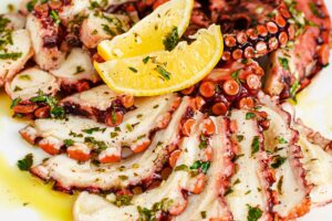 Piato da portata con sopra un. carpaccio di polpo condito con prezzemolo, olio e limone