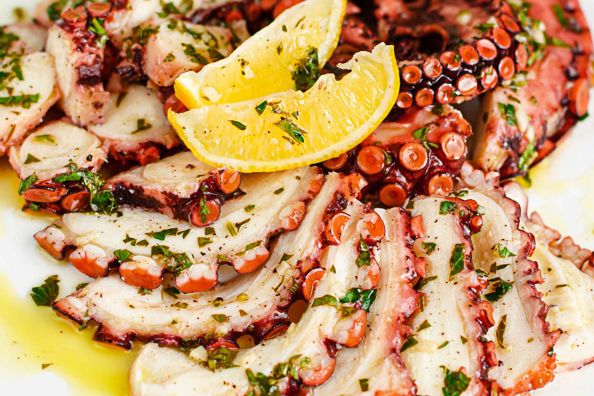 Piato da portata con sopra un. carpaccio di polpo condito con prezzemolo, olio e limone