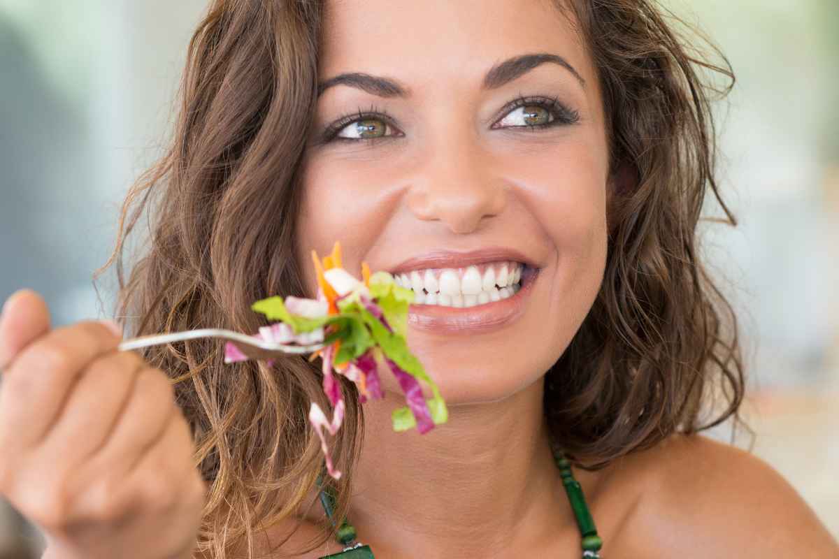 Ragazza felice che sorride mentre mangia l'insalata