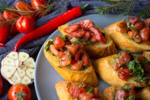 Bruschette al pomodoro in un piatto con intorno peperoncino, aglio e pomodori