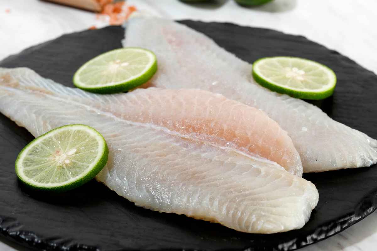 Pesce pangasio sfilettato su piatto da portata nero con delle fette di lime attorno