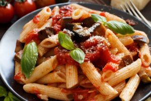 Primo piano di un piatto di pasta alla Norma fatto con le melanzane arrosto invece che fritte