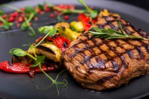 Piatto nero con all'interno una bistecca grigliata e delle verdure colorate