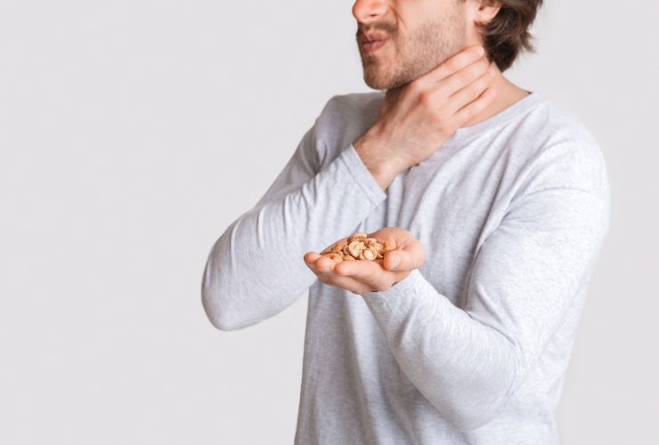 Hombre con la mano en la garganta y en la mano un alimento al que es alérgico